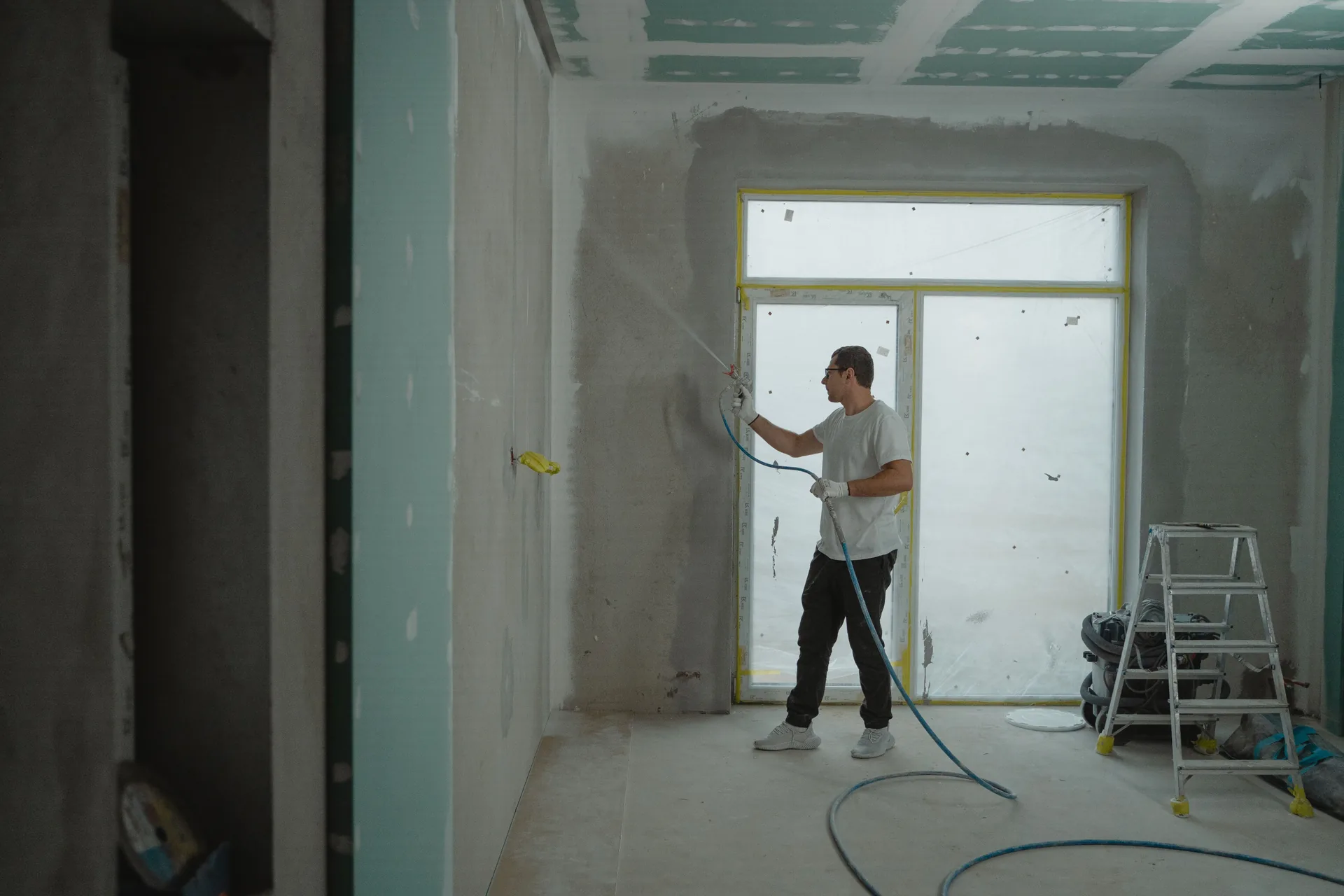 Painter spraying an interior wall in a room under renovation