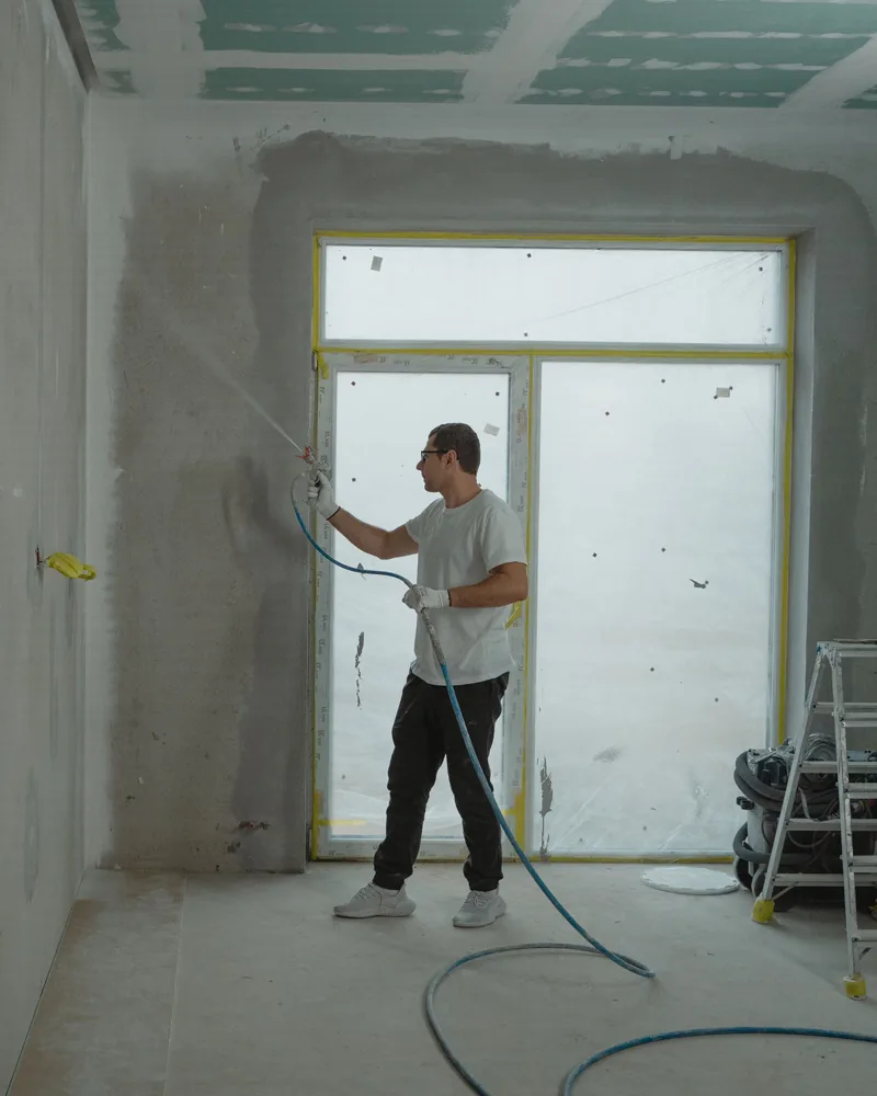 Painter spraying an interior wall in a room under renovation